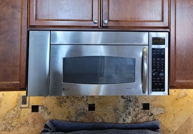 A stainless steel microwave oven is mounted above a granite counter top