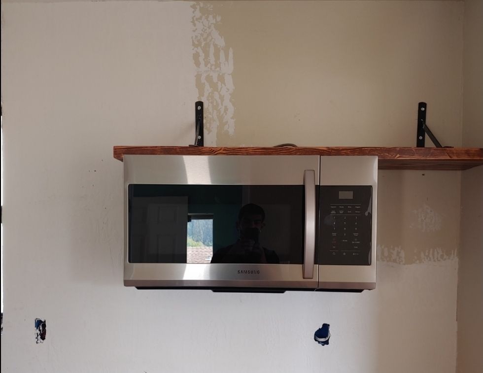 A stainless steel microwave with a wooden shelf above it