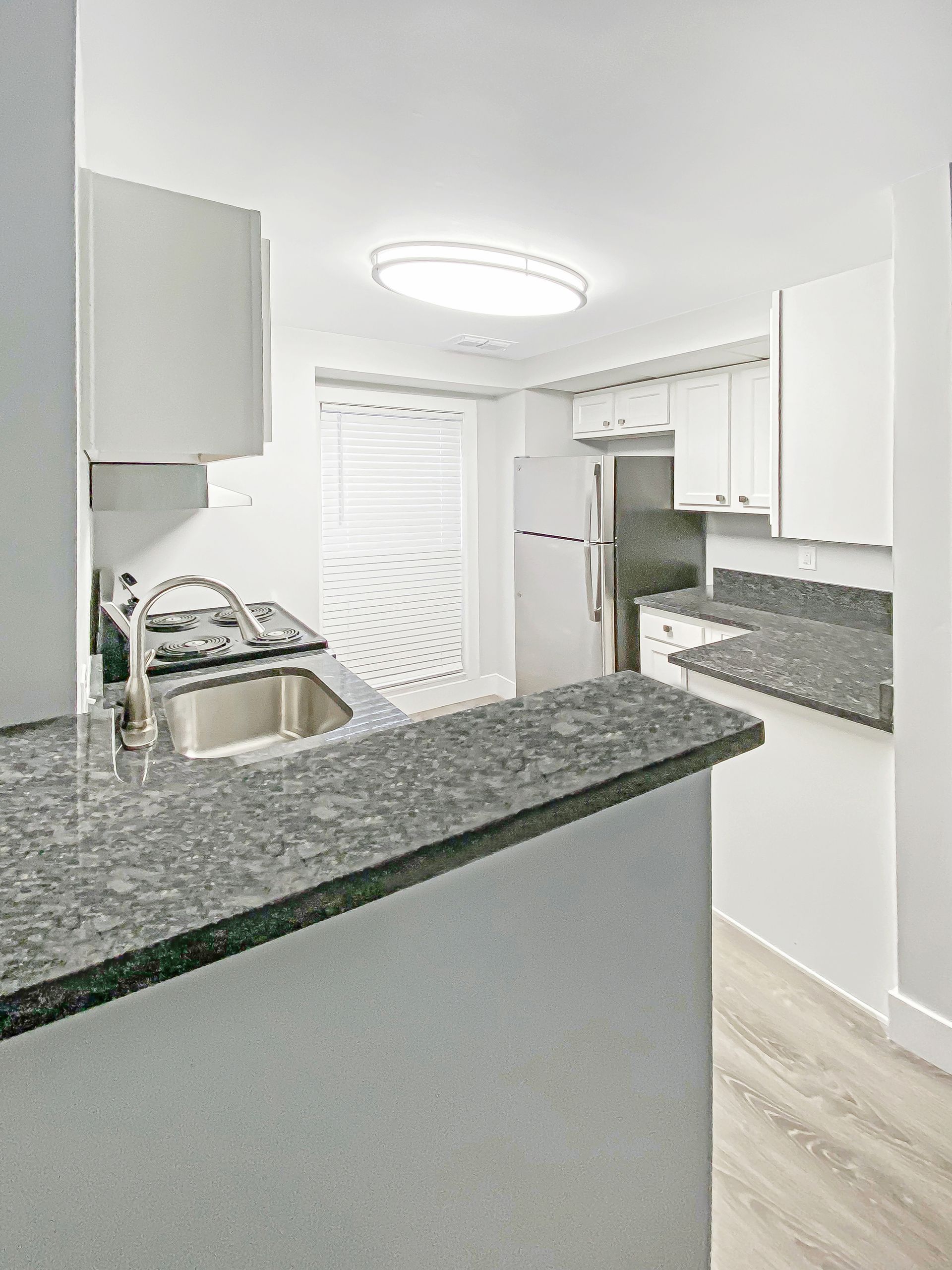 Bright modern kitchen with white cabinets, gray granite counters, stainless sink, and light wood flooring