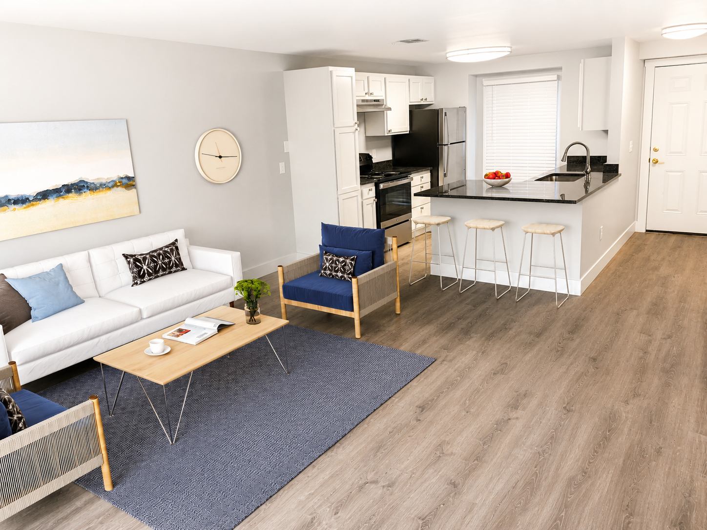 Bright open living room and kitchen with white sofa, blue rug, bar stools, and hardwood floors