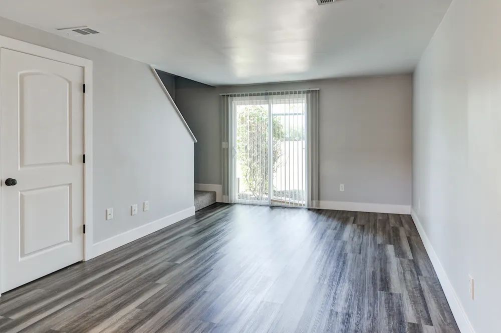 Empty room with gray wood floors, white walls, and sliding glass doors to a balcony