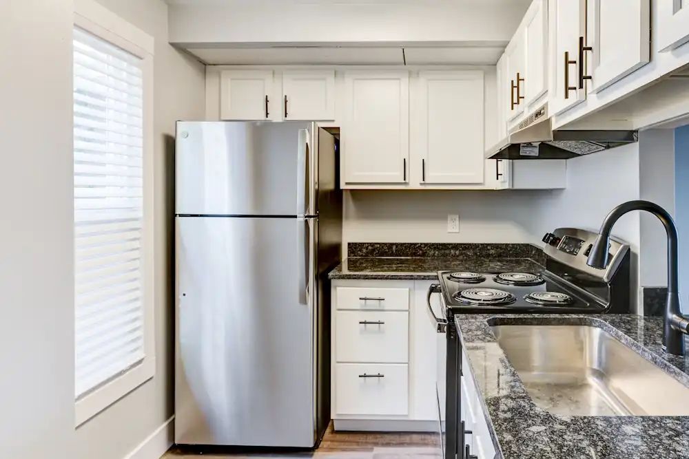 Small bright kitchen with stainless steel refrigerator, white cabinets, and granite countertops.