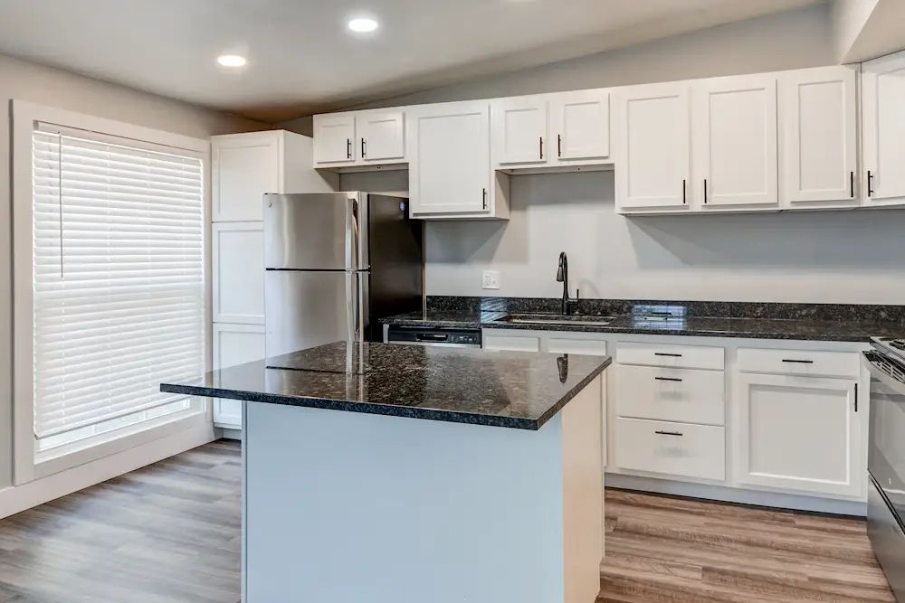 Modern kitchen with white cabinets, stainless steel appliances, dark granite counters, and a central island.