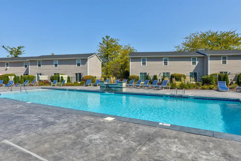 Outdoor swimming pool with blue water and lounge chairs in front of apartment buildings
