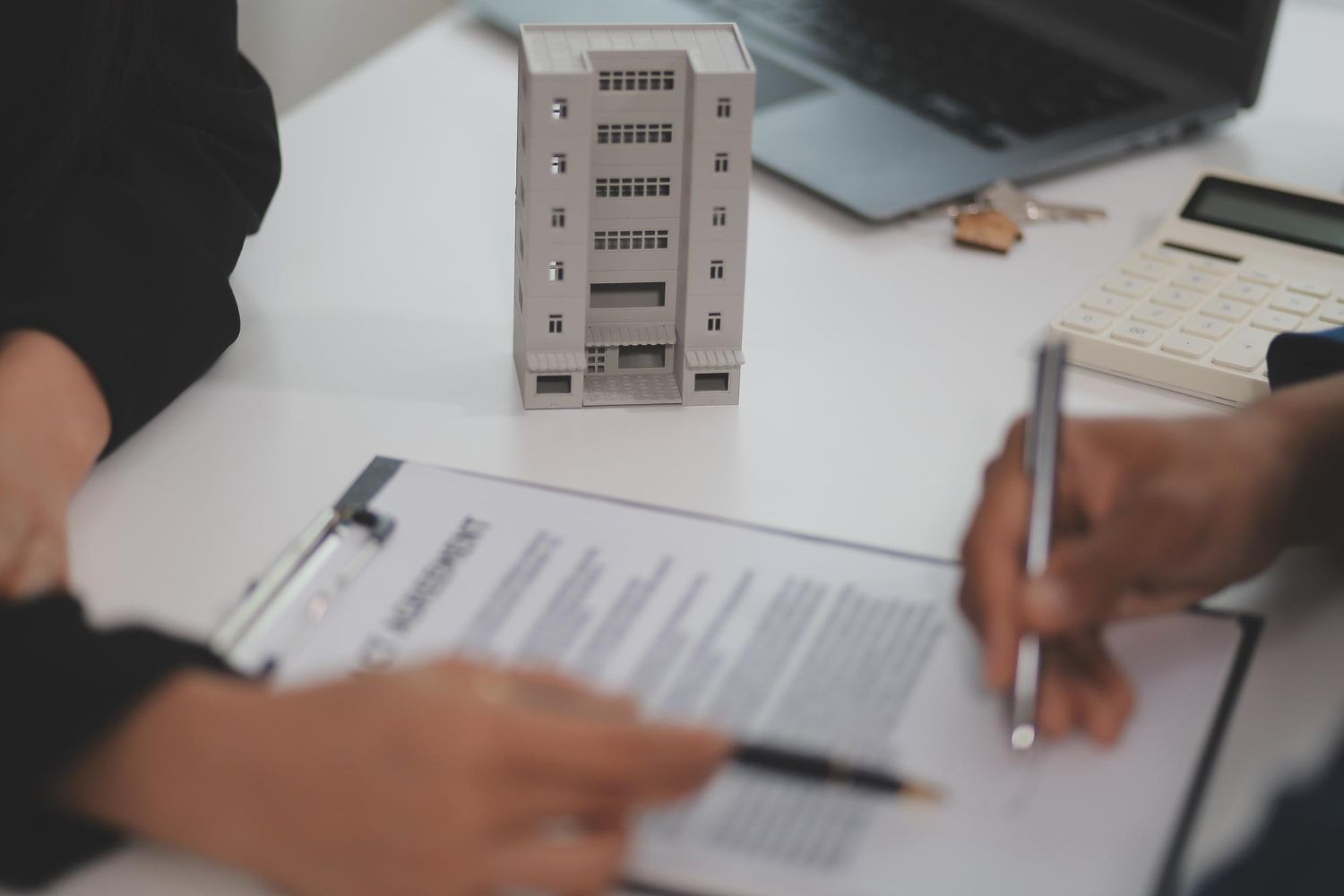 Two people review paperwork and sign a document beside a small building model on a desk