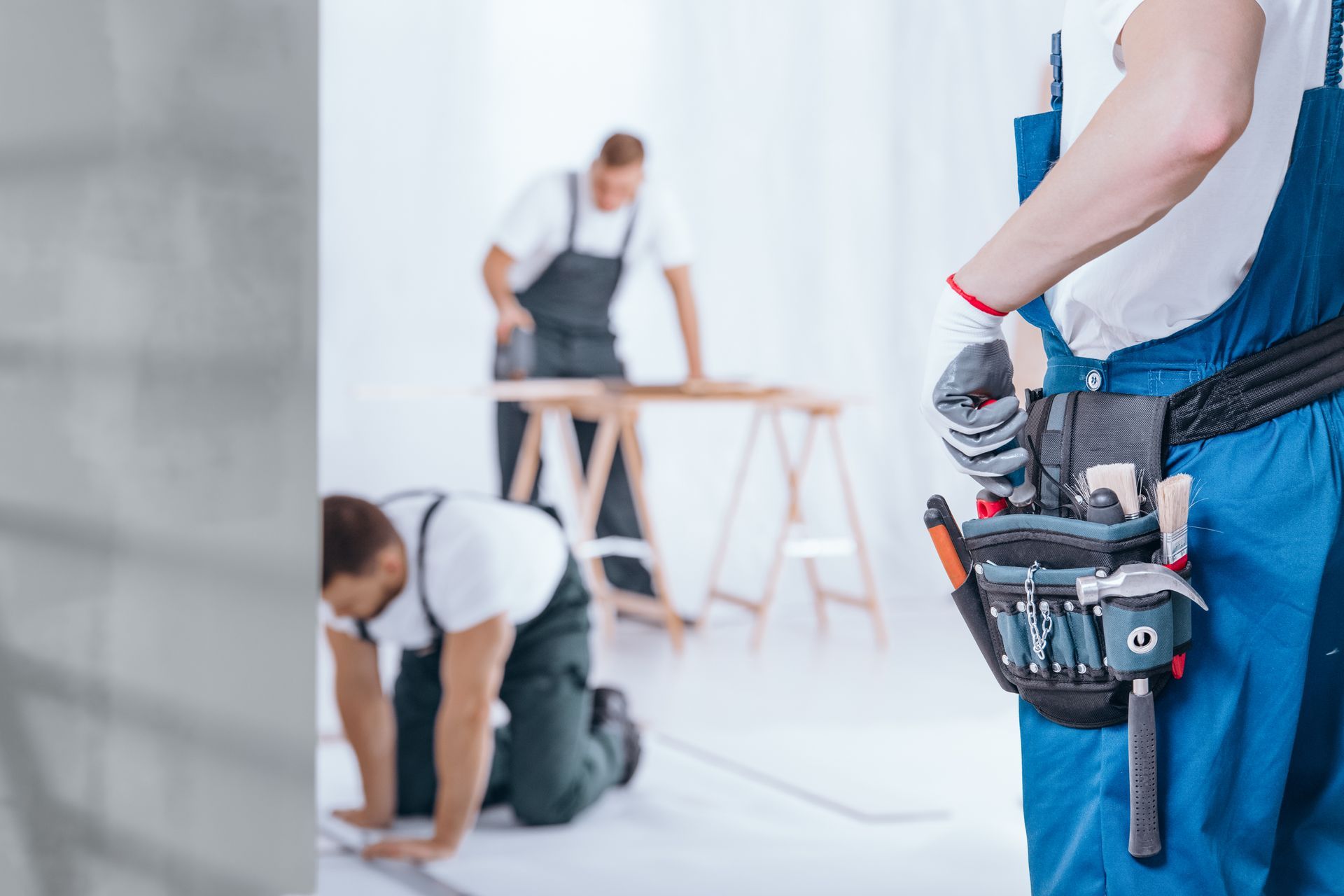 Construction workers in blue overalls working on a building site, with one person in the foreground wearing a tool belt.