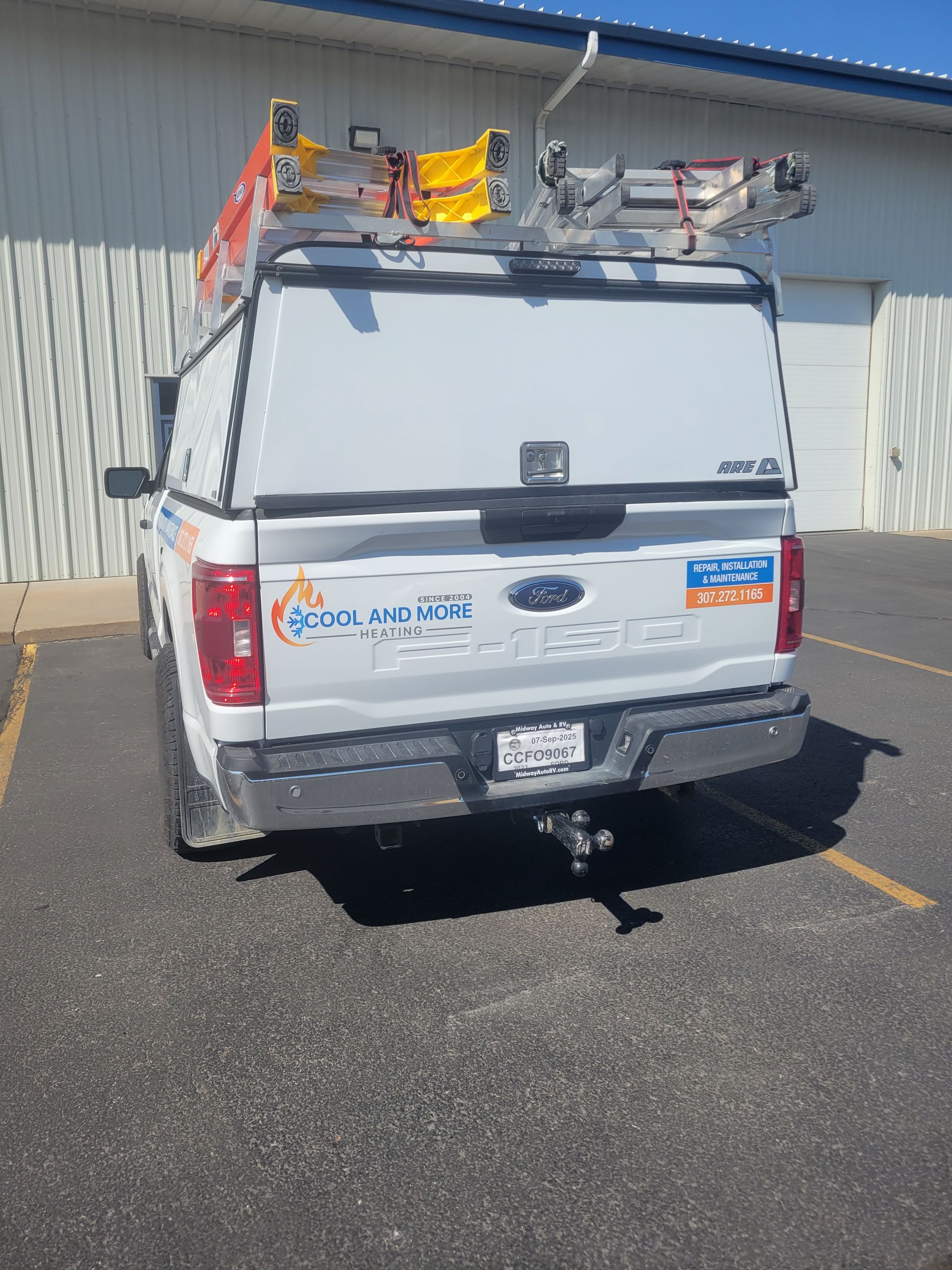 White utility truck with roof ladders parked in a lot beside a building.