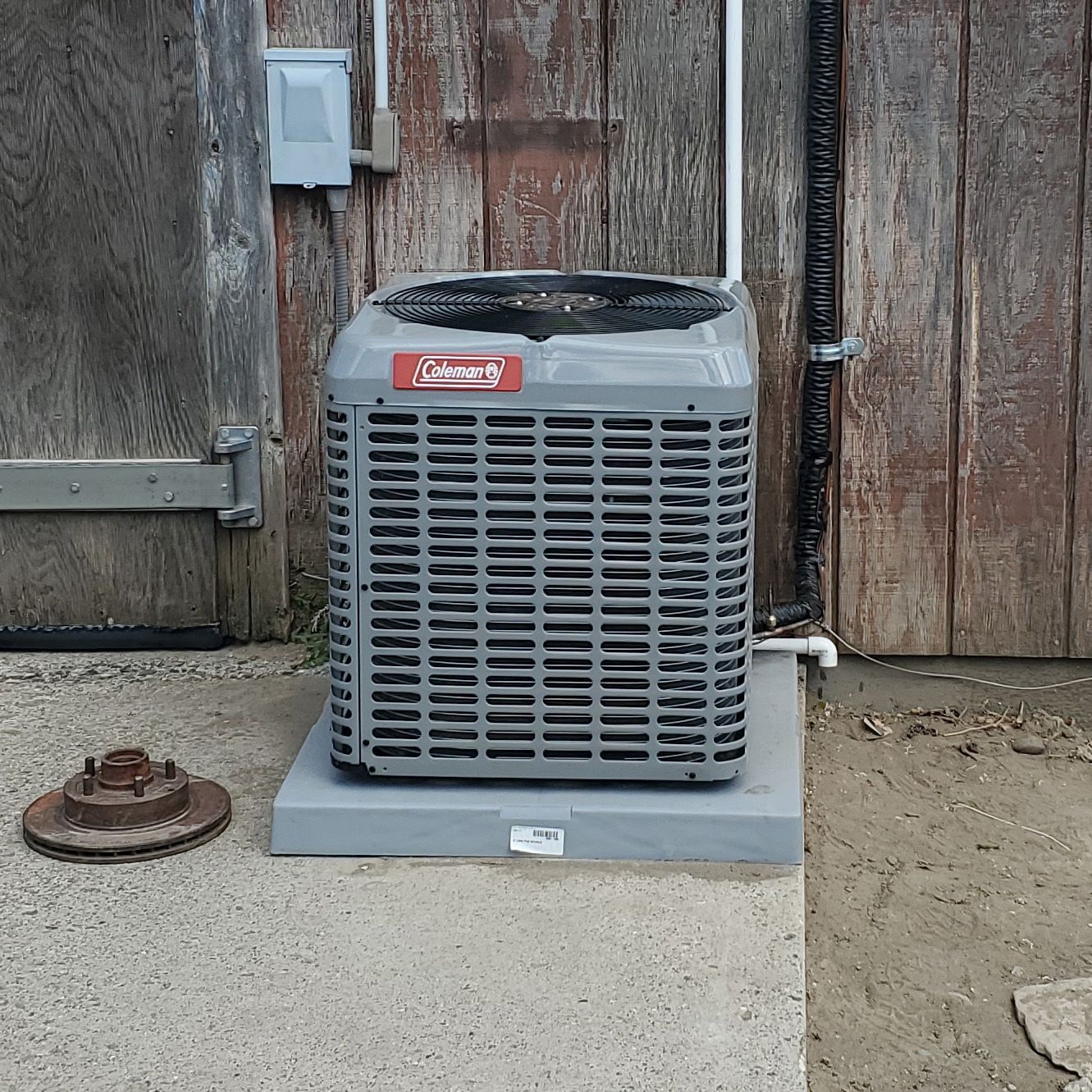 Gray outdoor air conditioner unit on a concrete pad beside a wooden fence and wall.