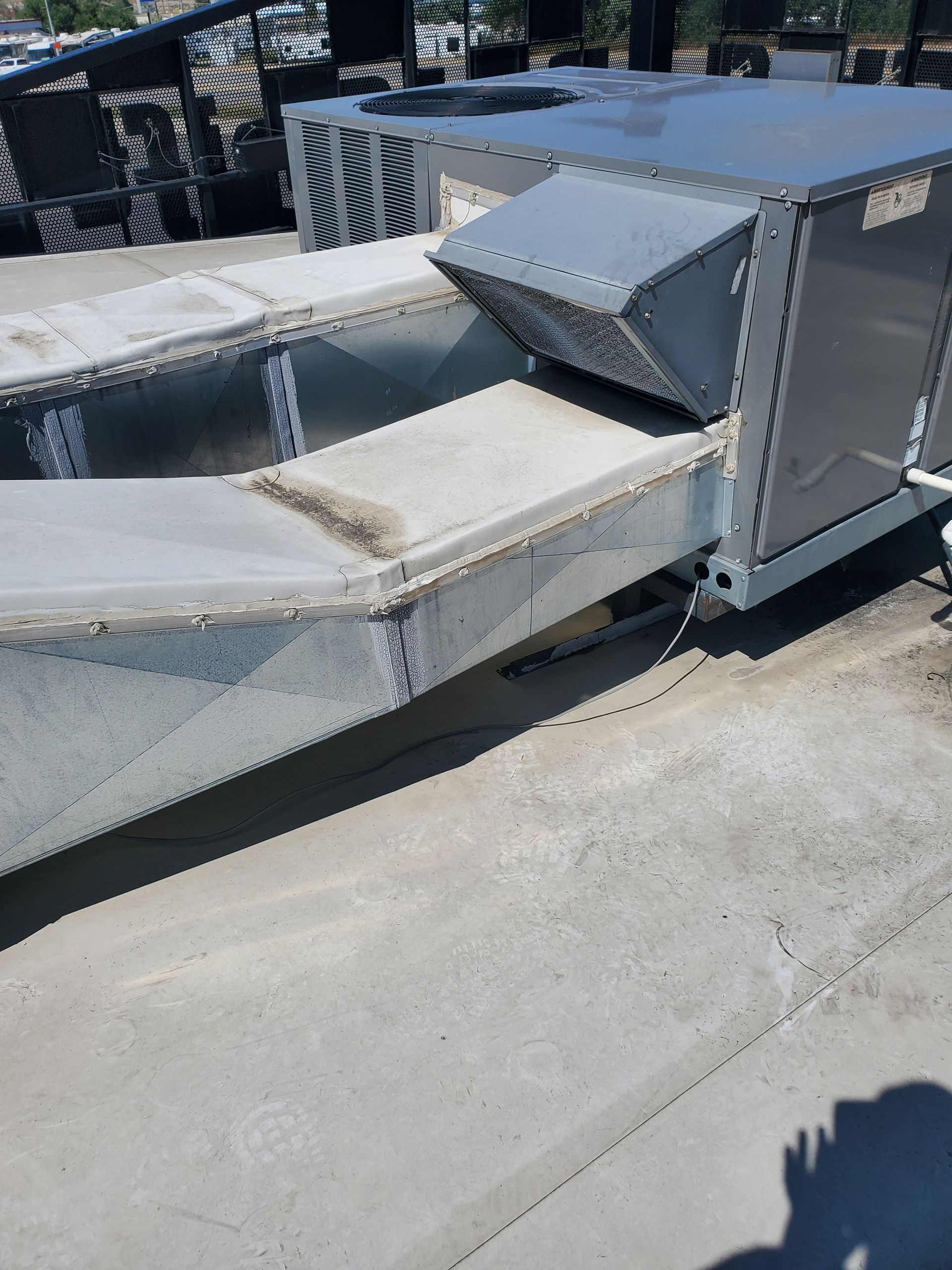 Metal industrial conveyor chute with a white sloped belt section and gray housing outdoors in sunlight