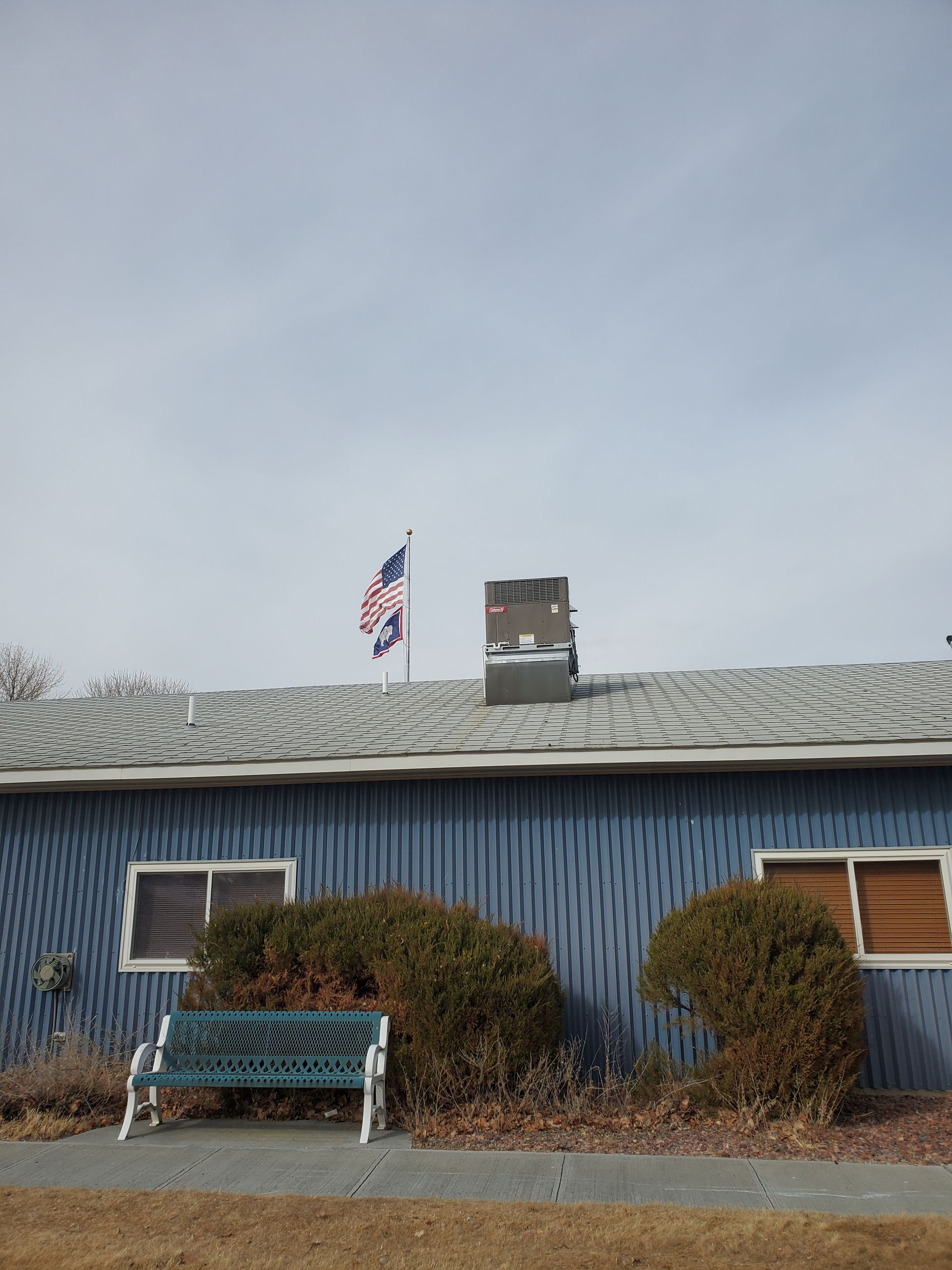 Blue house exterior with an American flag, small chimney, snowy roof, and a bench in front.