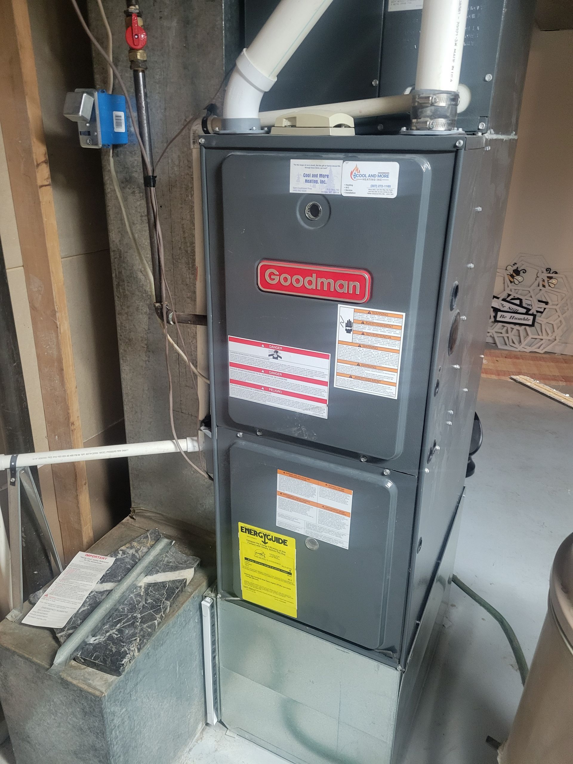 Gray furnace in a utility room with exposed ductwork and pipes.