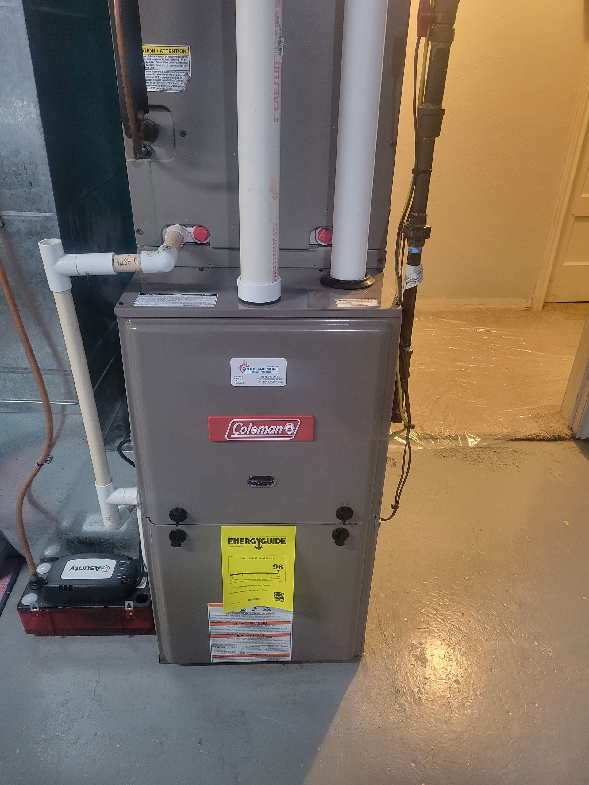 Gray furnace unit with pipes in a utility room beside a yellow wall and wet concrete floor