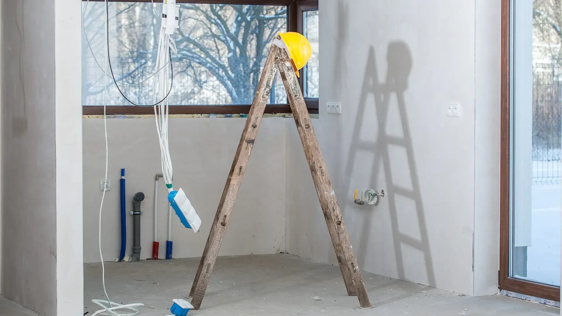 A wooden ladder is sitting in an empty room next to a window.