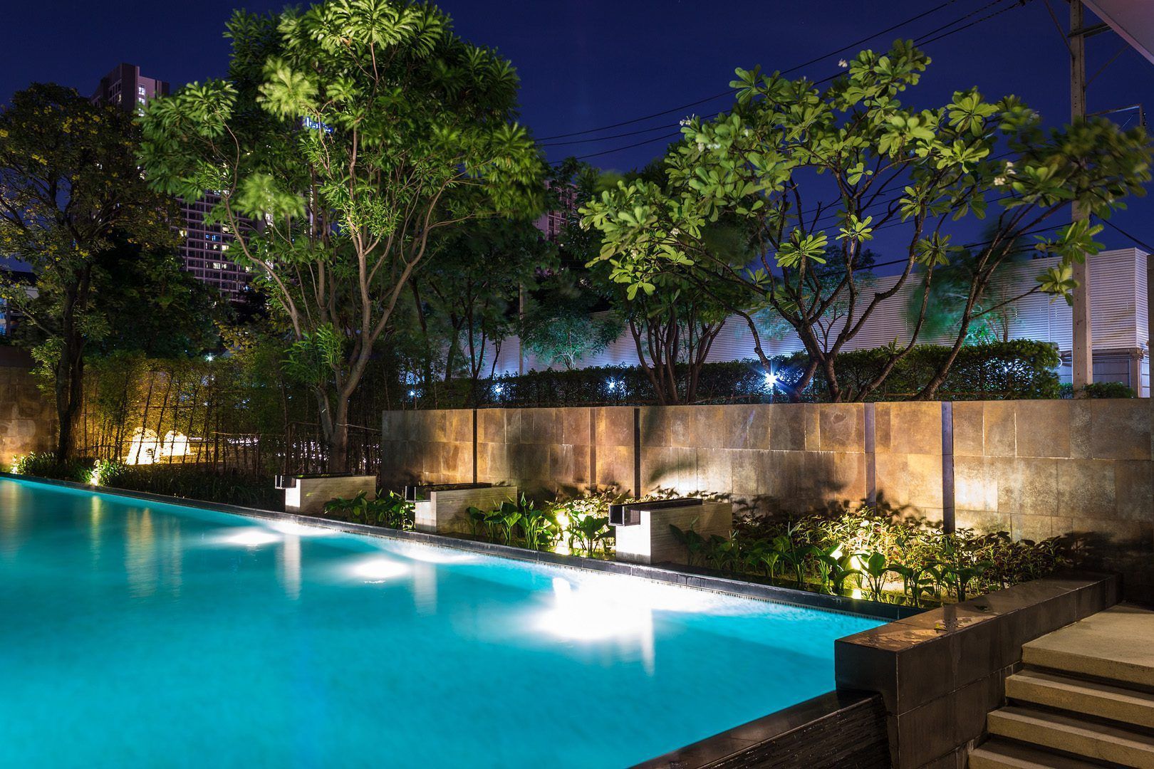 A large swimming pool is lit up at night with trees in the background.