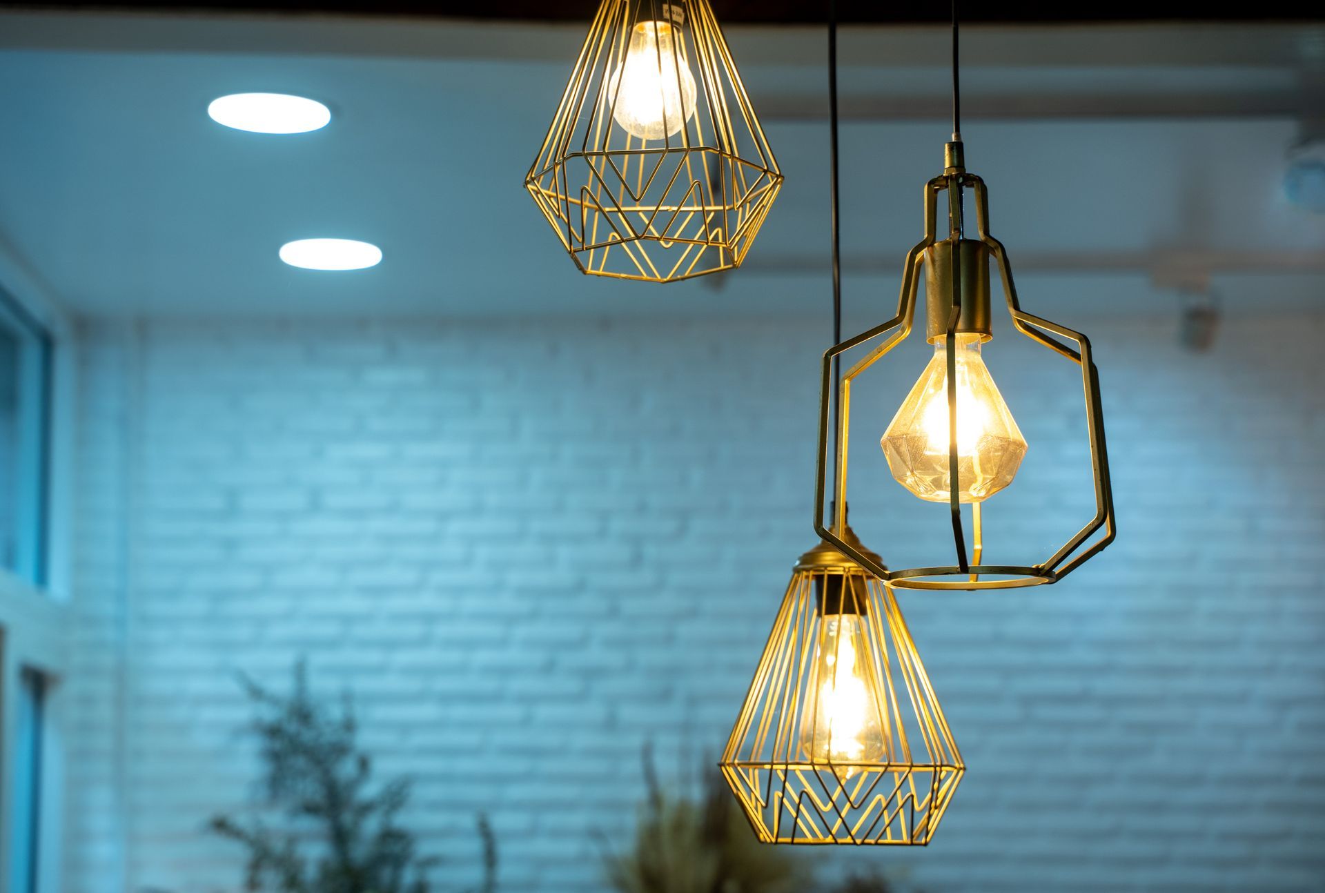 Three geometric pendant lights glowing over a blue-tiled interior wall