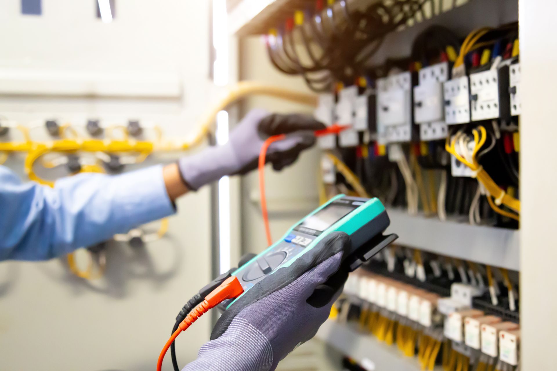 Gloved technician testing electrical panel with handheld meter and wires in a workshop