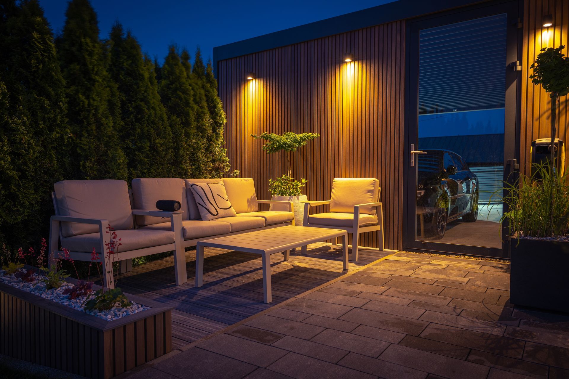 Cozy outdoor patio with beige lounge chairs, warm lights, and potted plants beside a modern building