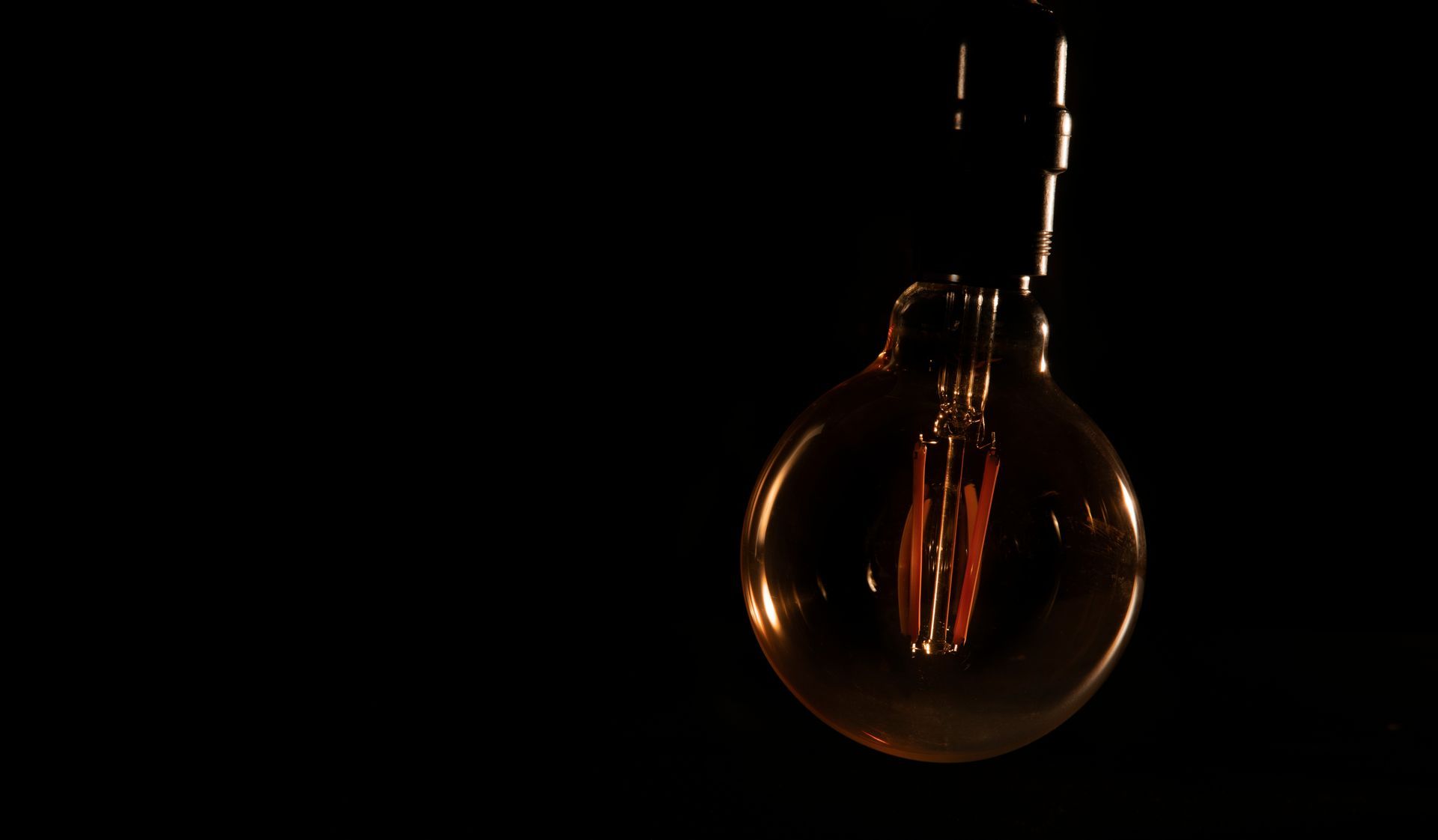 A lit incandescent bulb glowing against a dark background, with its cord visible above.
