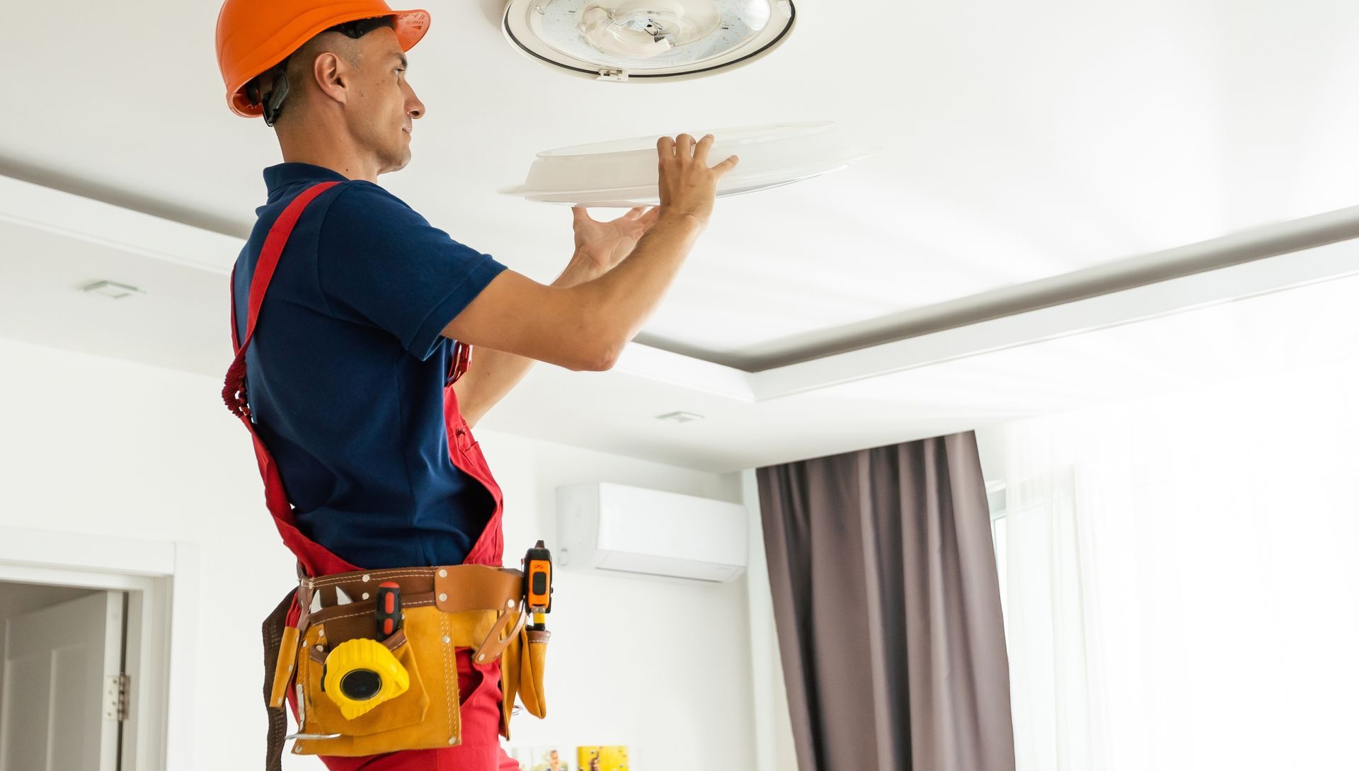 A man is installing a light fixture on the ceiling of a living room.