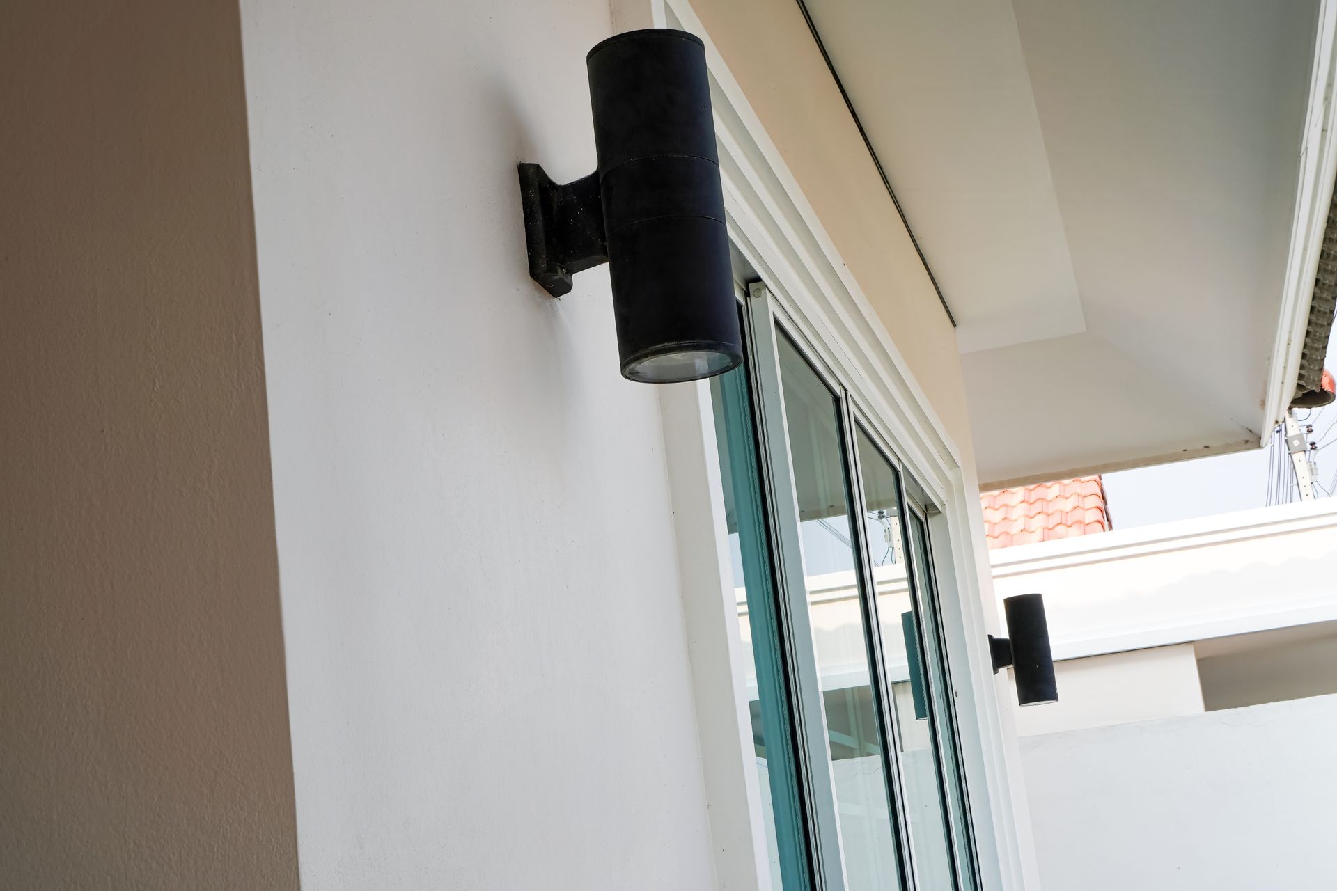 Black wall-mounted cylindrical light beside a sliding glass door on a balcony walkway