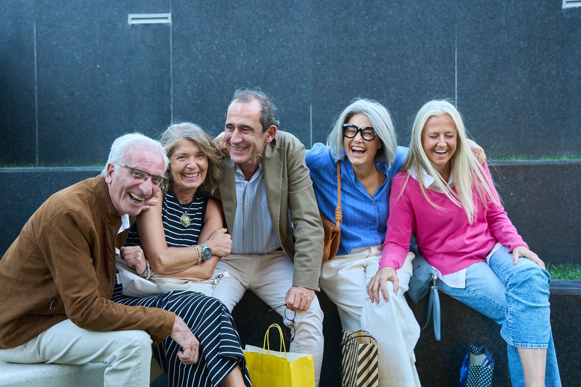 Five smiling friends sitting on steps outdoors, leaning close together and laughing.