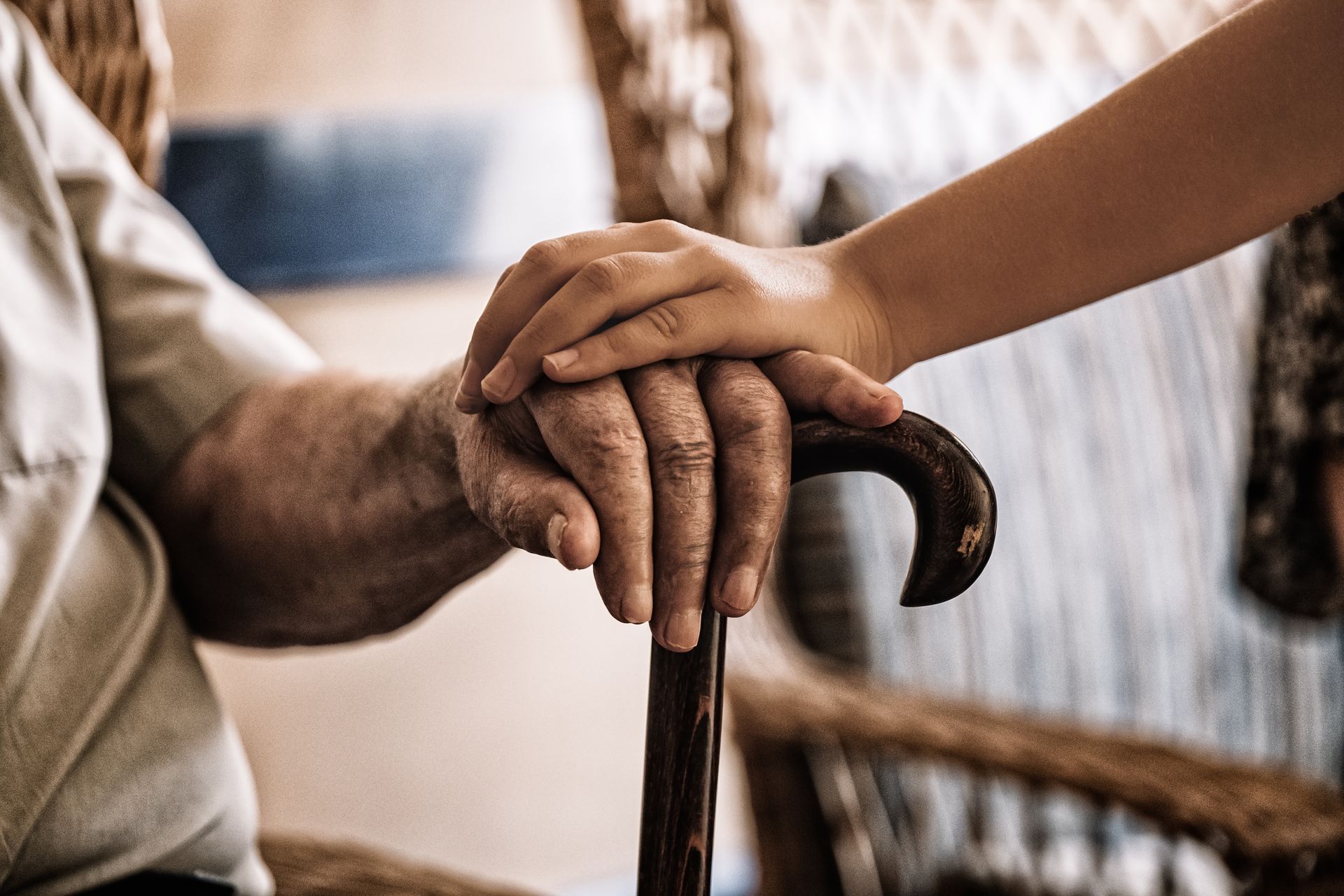 Two hands resting on a wooden cane, with a blurred indoor background