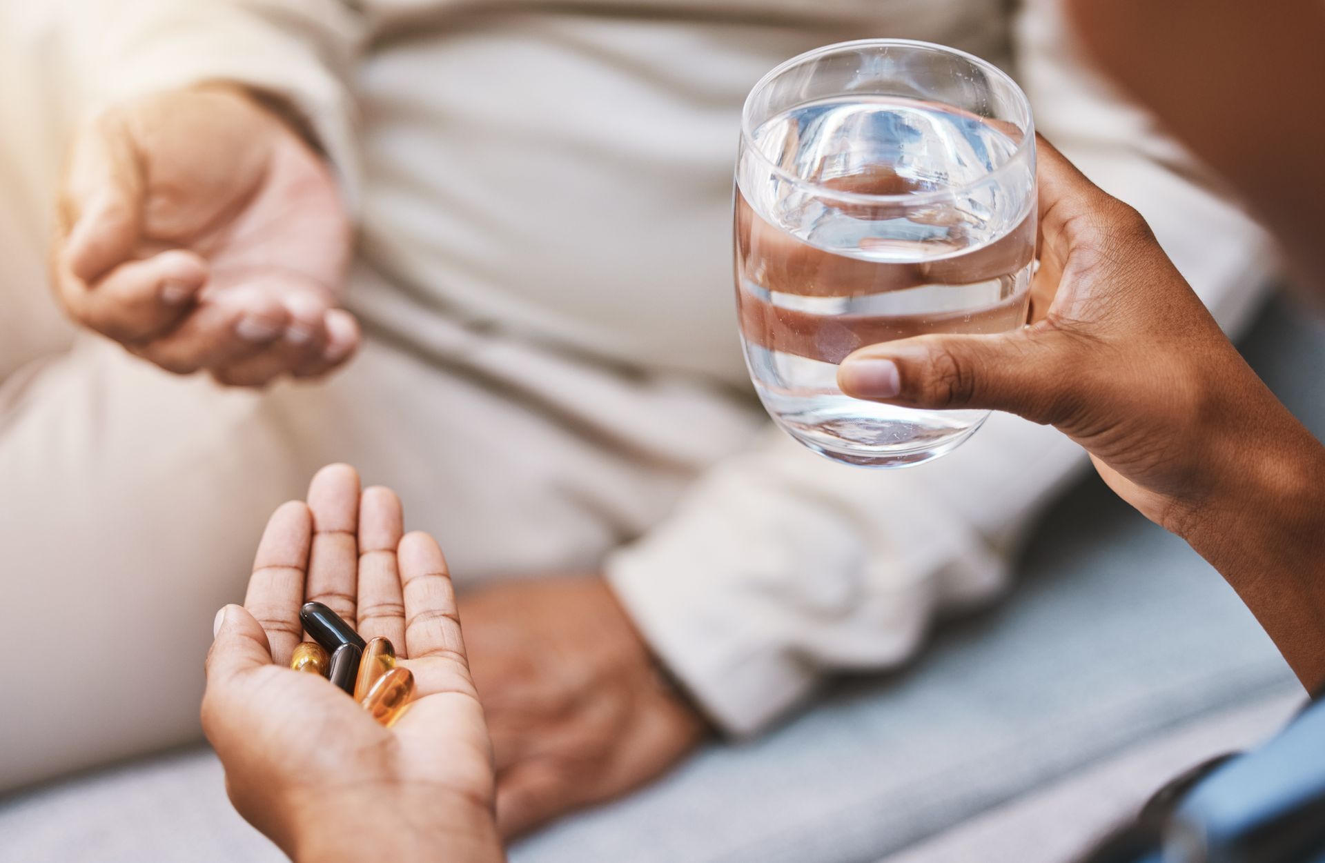 Person holding pills offering them to another person with a glass of water. Person holding pills offering them to another person with a glass of water.