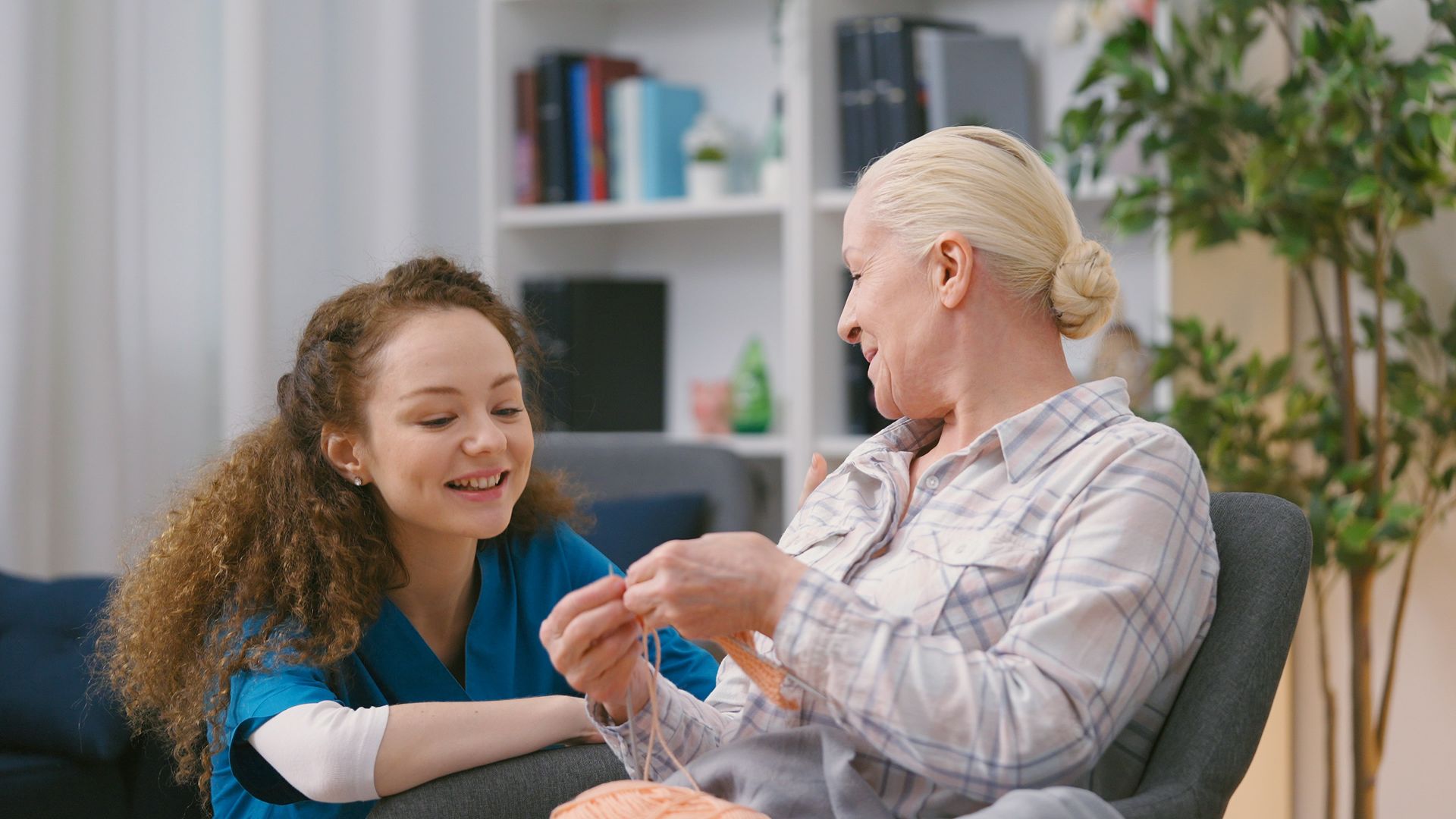 Two people smiling and chatting while wrapping a bandage on a forearm in a bright living room