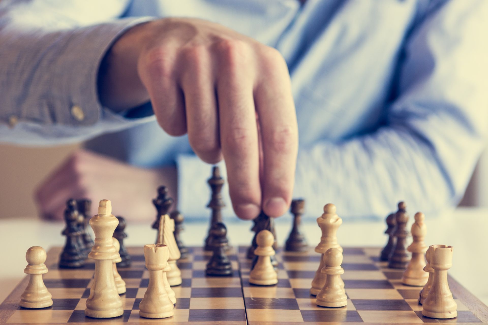 Hand moving a chess piece over a chessboard with white and black pieces Hand moving a chess piece over a chessboard with white and black pieces