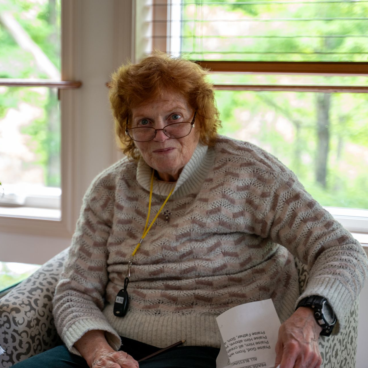 Woman sitting by a window holding a paper, wearing a cream sweater and glasses. Woman sitting by a window holding a paper, wearing a cream sweater and glasses.