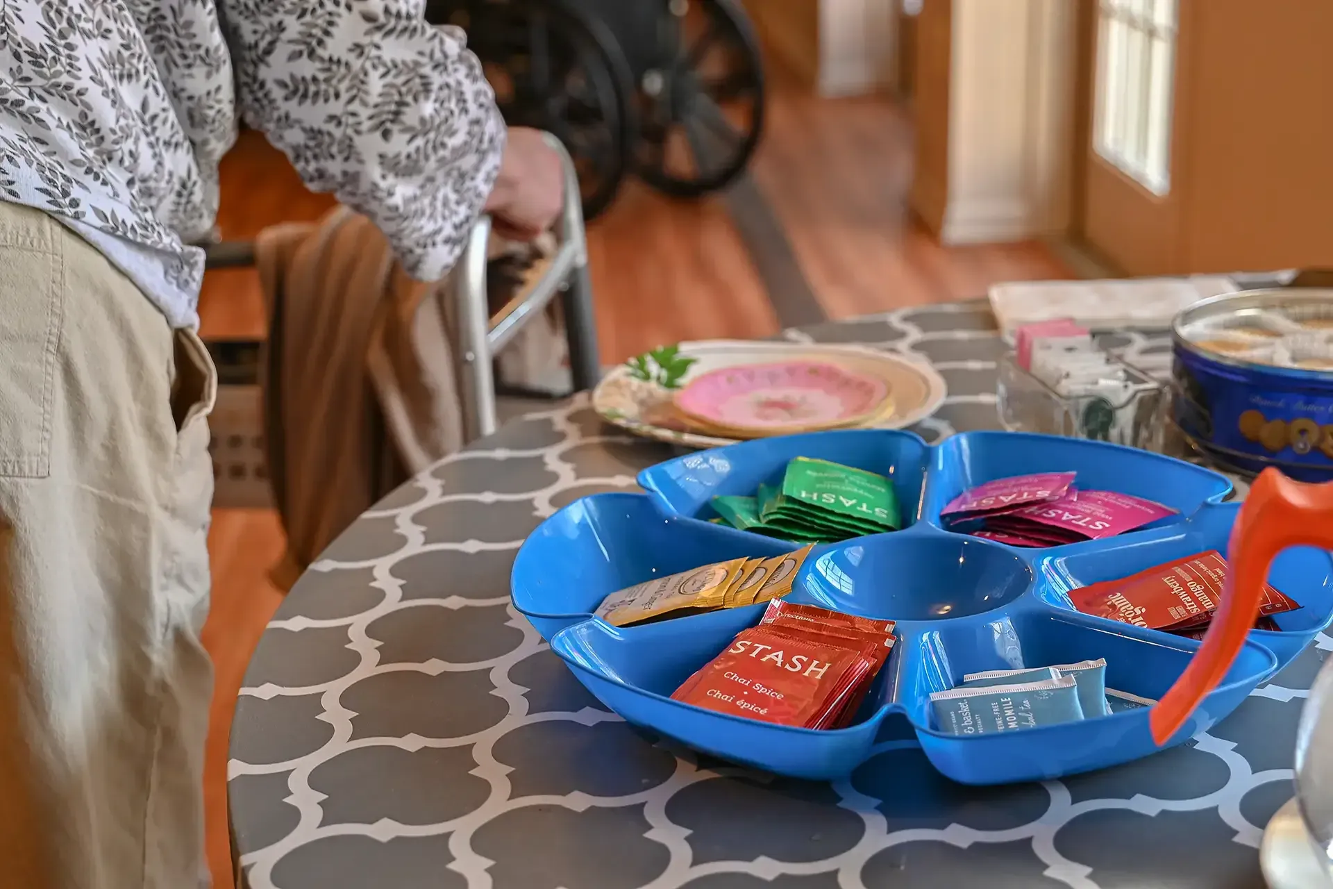 Person using a walker at a table with a blue divided serving dish holding colorful packets.