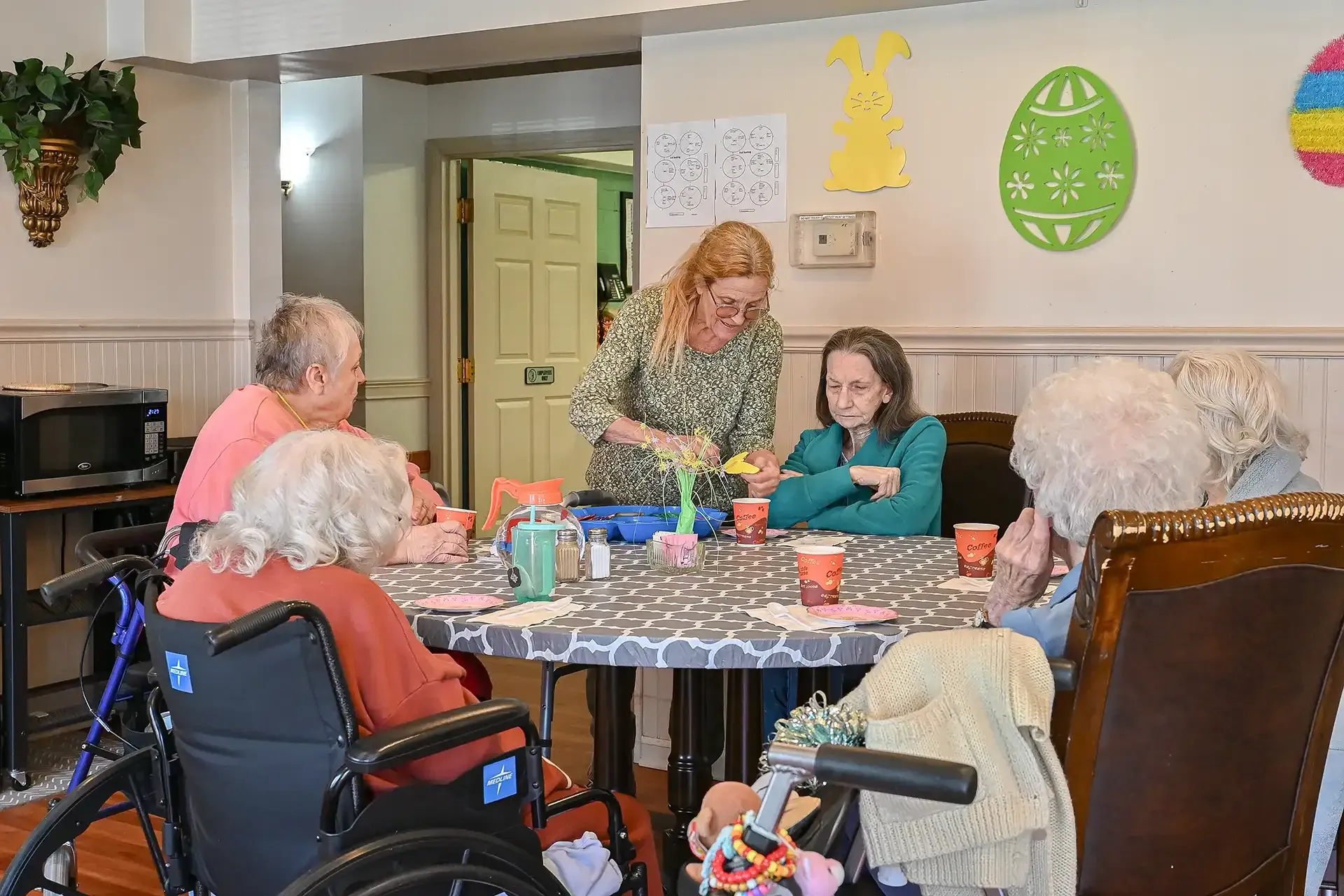 A group of seniors craft at a table with an instructor in a decorated room.