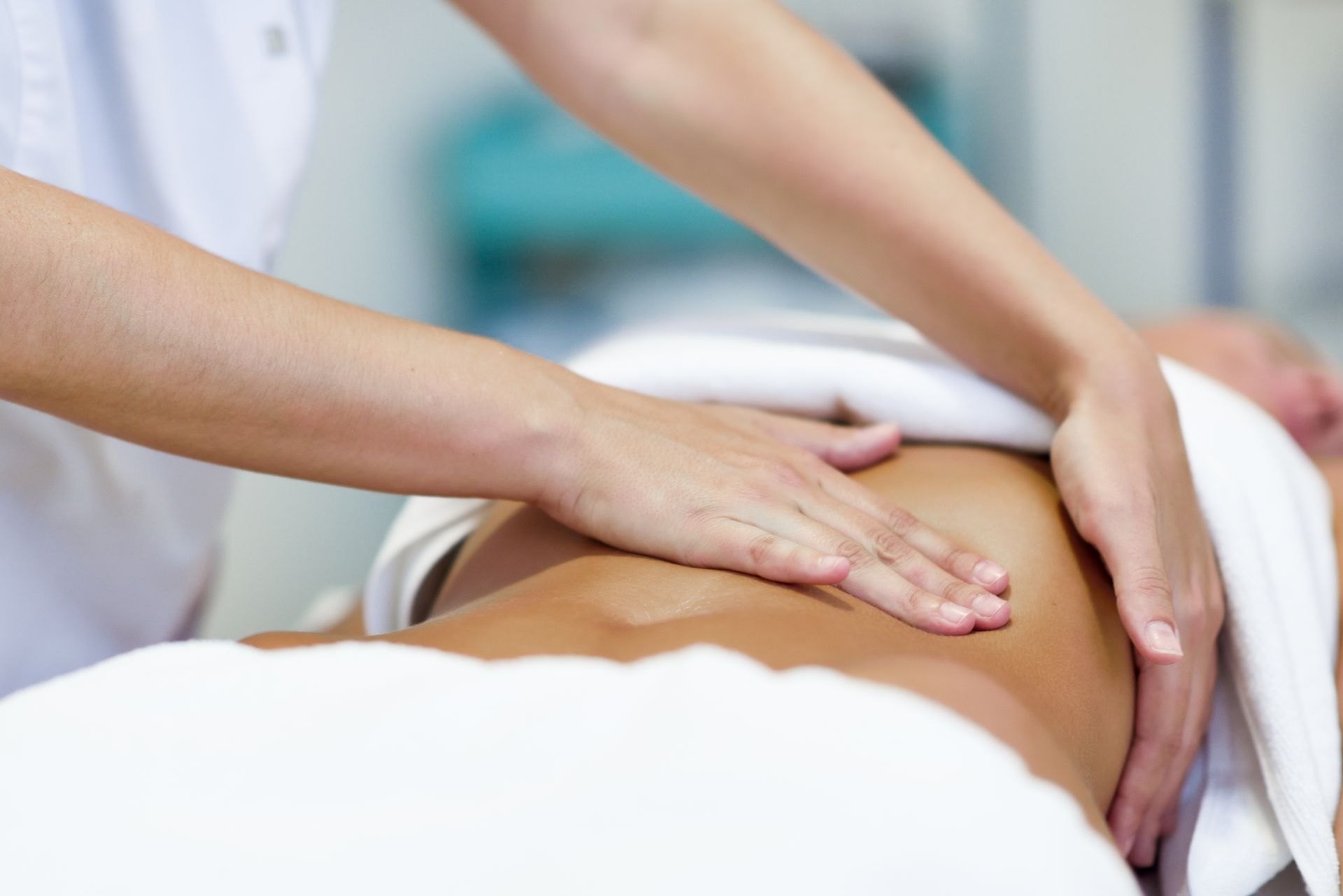 Masseur gibt einer Person, die mit einem Handtuch bedeckt auf einem Tisch liegt, eine Bauchmassage.