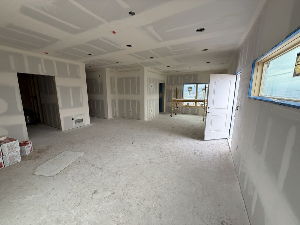 Unfinished drywall interior of a new home with white walls, ceiling, and construction materials on the floor
