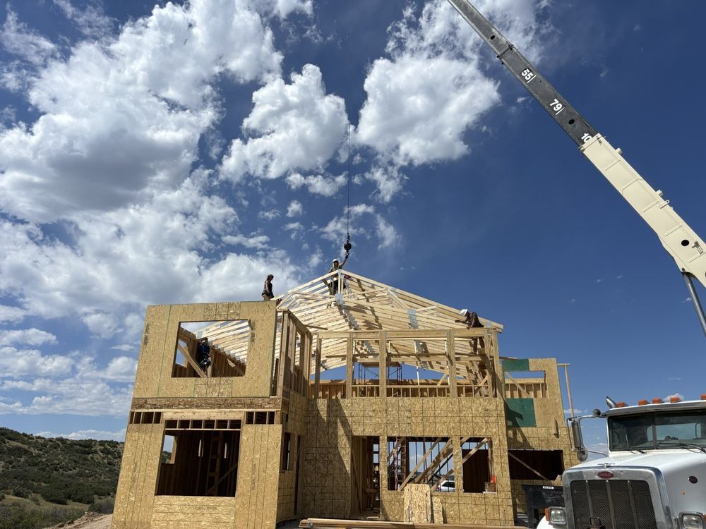 Wood-framed house under construction with crane against a blue sky and clouds