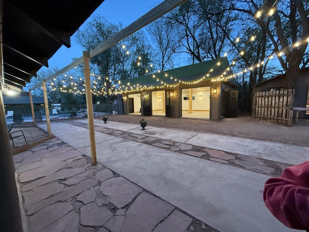 String lights over a small outdoor patio with a wooden building at dusk, and stone paving in the foreground
