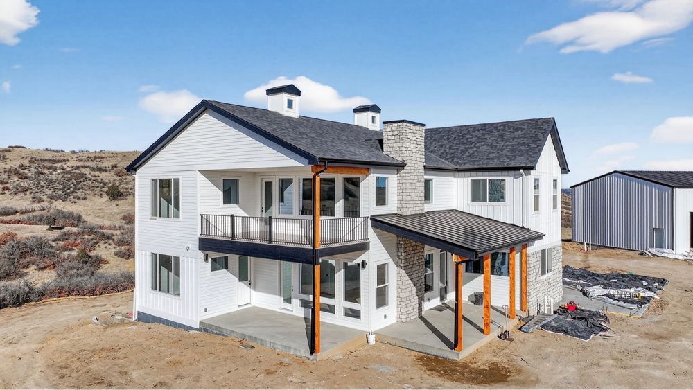 White two-story house with dark roof and balconies under construction in a desert setting