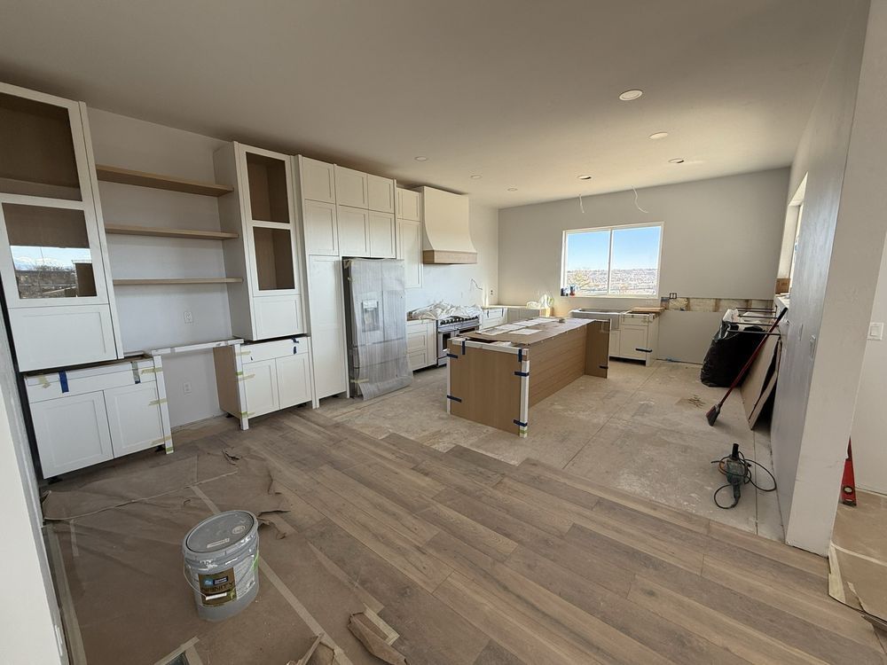 Unfurnished kitchen with white cabinets, wood floors, boxes, and a sink by a bright window.