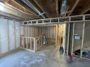 Unfinished basement with exposed beams, framed walls, ladder, and construction materials on the floor