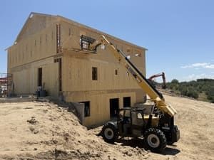 Construction site with a large wooden house frame and a yellow crane lifting materials.