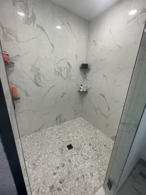 Small marble-tiled walk-in shower with white walls, speckled floor, and glass door.