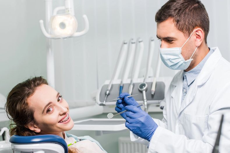 Dentista examinando a un paciente sonriente en un sillón dental con guantes azules y mascarilla.