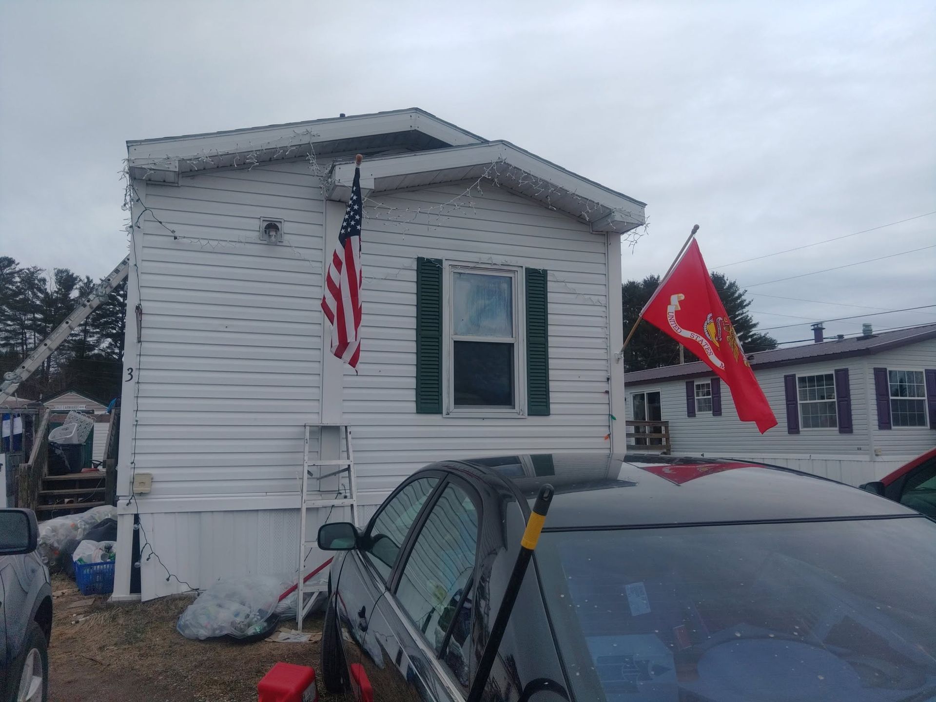 Mobile home with American and Marine flags, seen over a parked car in a snowy yard