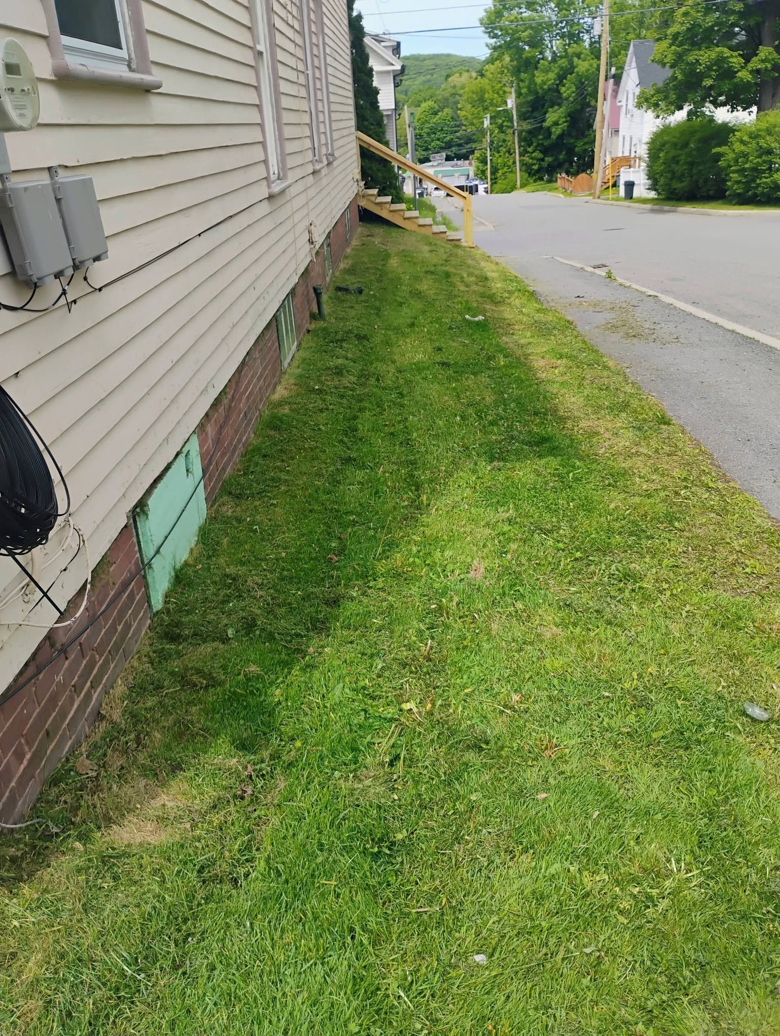 Narrow grassy strip beside a beige house along a quiet residential street