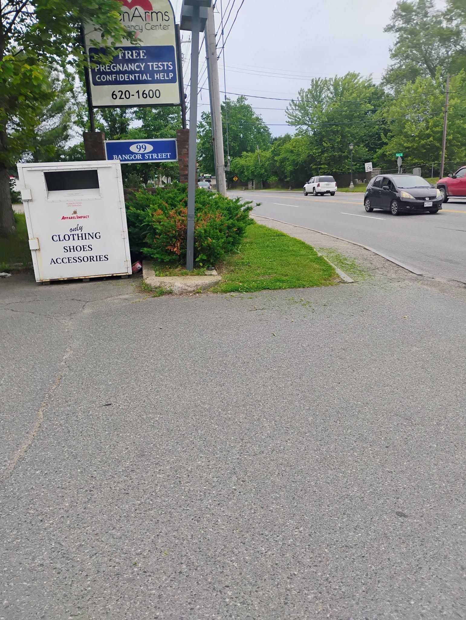 Roadside scene with a white trash bin, signs, and cars on a curving wet street under cloudy skies