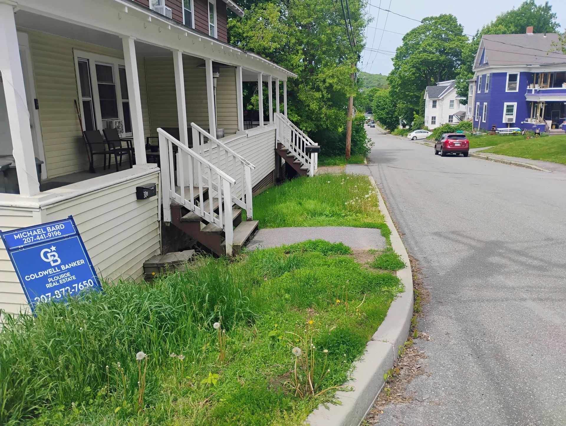 White house porch with ramp and blue accessibility sign beside a quiet residential street