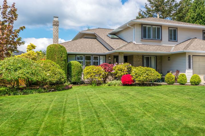 Suburban house with a manicured green lawn, colorful shrubs, and a partly cloudy sky