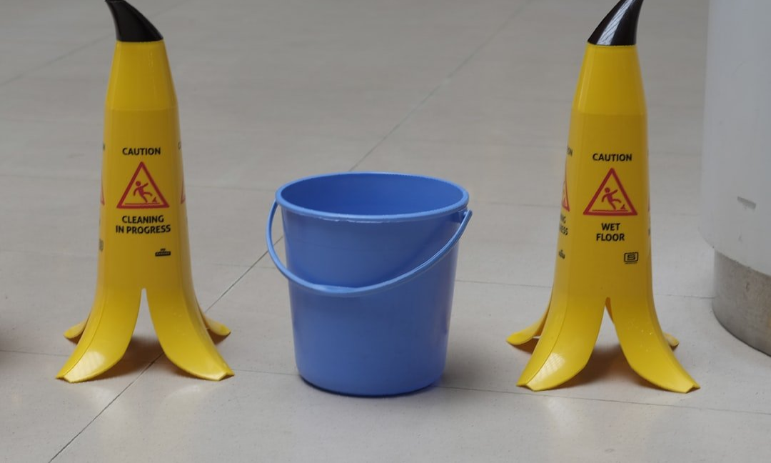 Two yellow caution cones flank a blue bucket on a tiled floor.