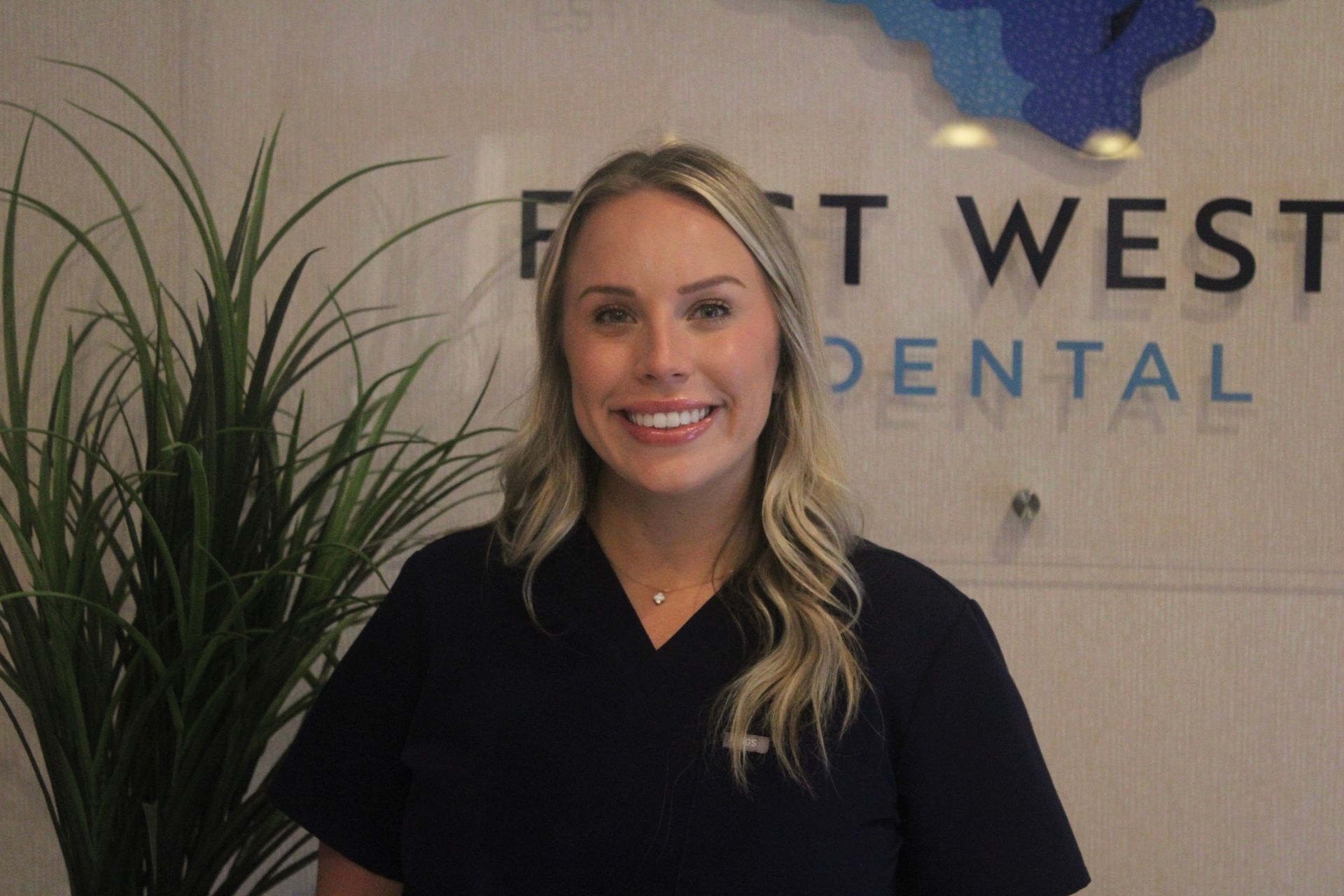 Woman in dark blue scrubs smiles in front of