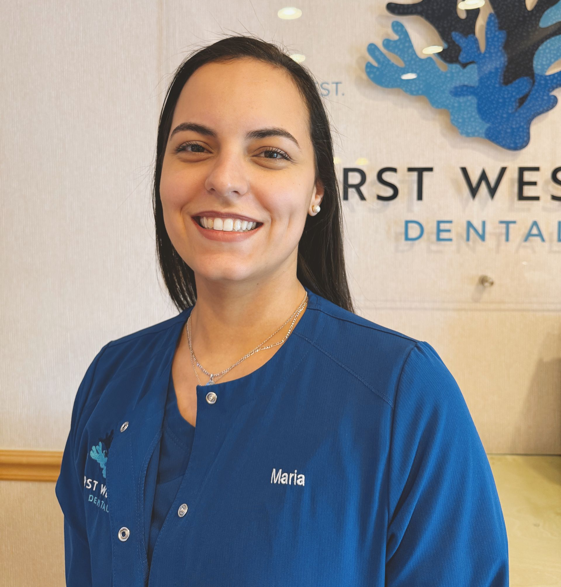 Woman in blue scrubs smiles in a dental office;